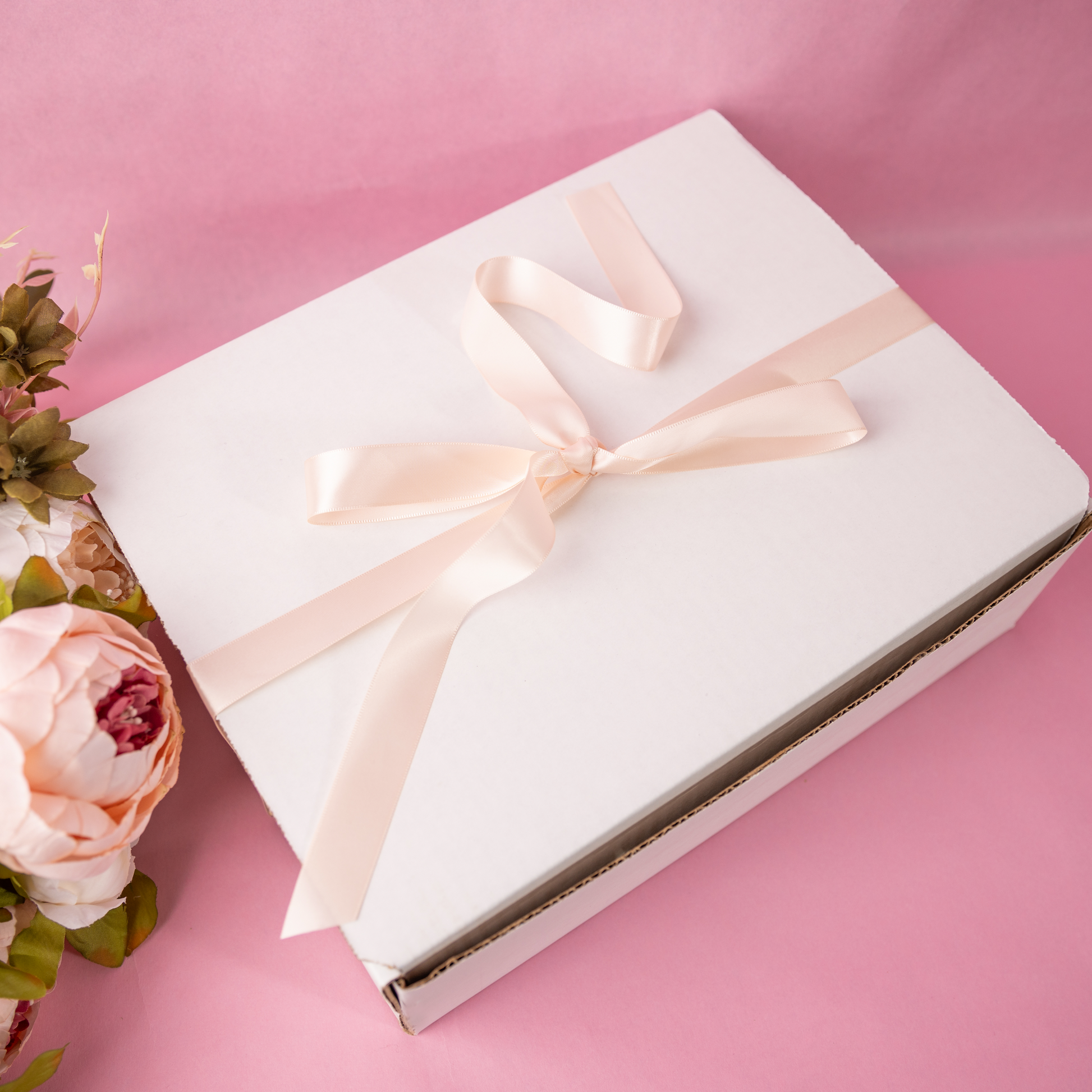 a white box with a pink ribbon and a bouquet of flowers