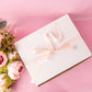 a white box with a pink ribbon and flowers